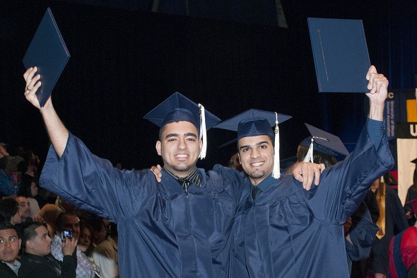 Two graduates hold up their diplomas