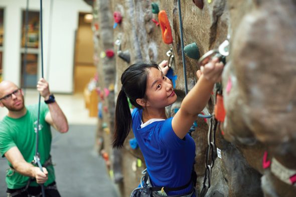 young woman climbing a rock wall, man in the background belaying