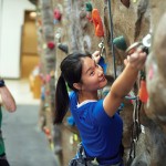 young woman climbing a rock wall, man in the background belaying