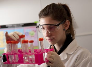 woman looking at test tubes, wearing goggles and white jacket