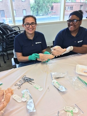 Lisbeth Perez from Nicholas Senn High School and Estrella Rivera from Roberto Clemente Community Academy show off their suturing skills on chicken breasts.