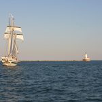 A tall ship on Lake Michigan with lighthouse in the distance