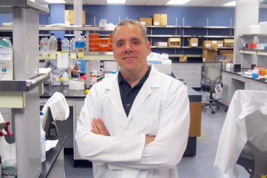 Jeremy J. Johnson, Associate Professor standing in lab with arms folded.
