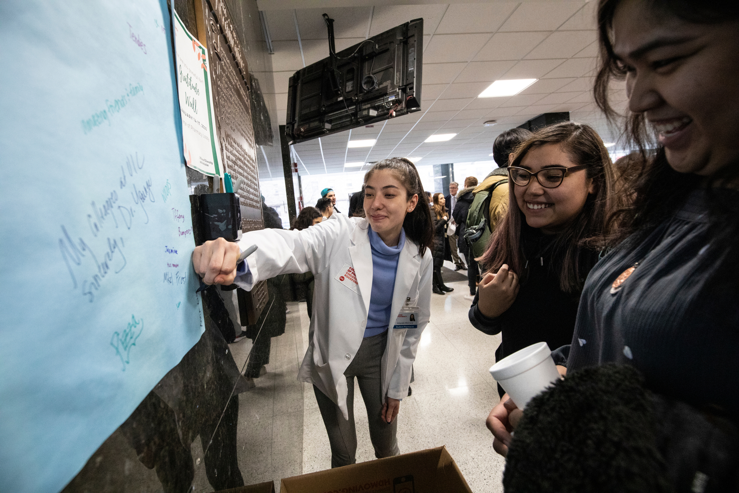 Amanda McCrone (PHARM '23), center, writes the names of her friends, Yoselin Flores and Anna Lisa Russell, right, on a "gratitude wall" during a welcoming event for pharmacy students at the college.