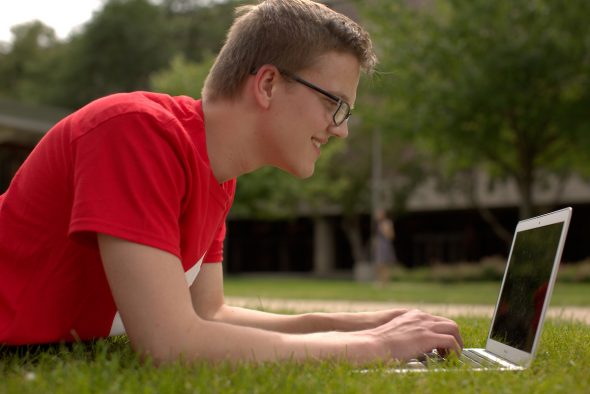 male student lying in the grass with laptop (