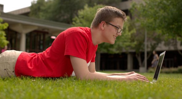 Male student laying in the grass using a laptop