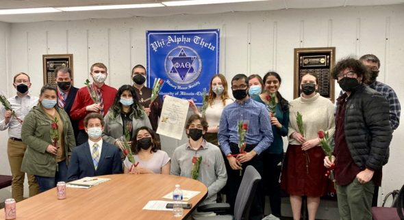 Students wear masks and hold red roses as they are inducted into Phi Alpha Theta History Honors Society.