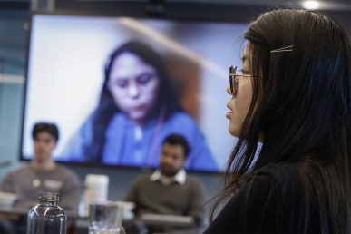 A student (Trish Le) sits at a table in a conference room with Morning star employees participating in a virtual meeting.