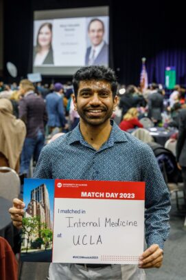 A man poses with a sign listing his residency match.