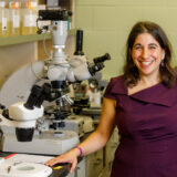 A photo of Dr. Rachel Poretsky next to some microscopes taken by Ian Battaglia.