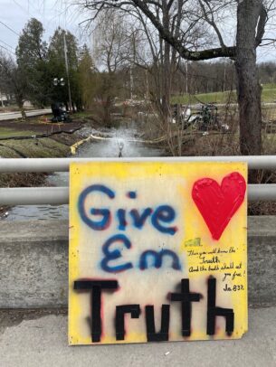 Sulphur Run, a waterway near the derailment site in East Palestine, Ohio, has a large sign in front of the river that says "Give em truth."