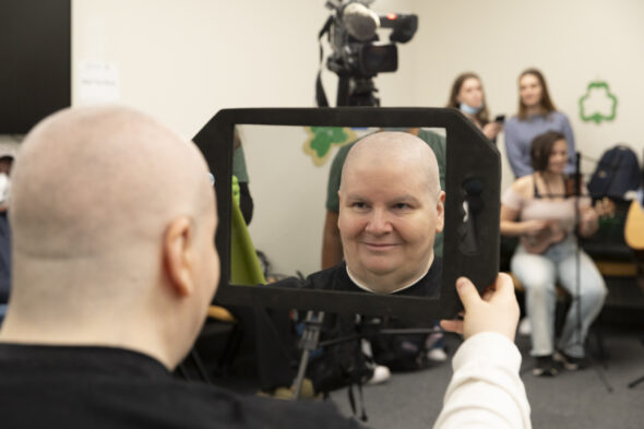 A woman with a newly shaved head looks at her reflection in a mirror.