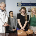 A woman practices CPR on a dummy as others look on and offer guidance.