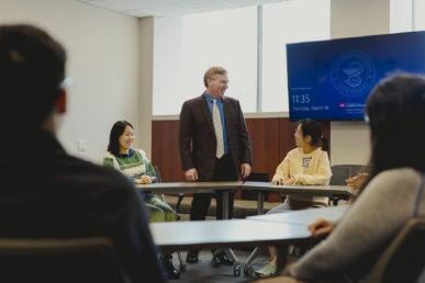 A man faces students in a conference room