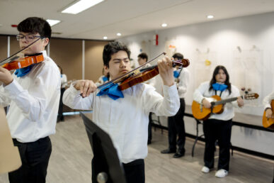 Several high School students holding violins and guitars practice mariachi music