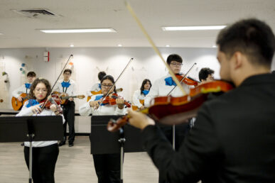 Several high School students holding violins and guitars practice mariachi music