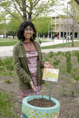 A student smiling behind a sign on a planter