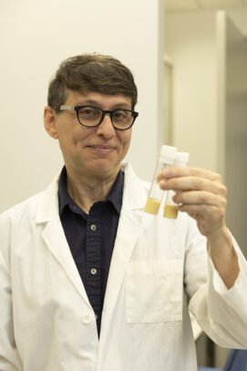 A man in a white lab coat and glasses holds up two test tubes.