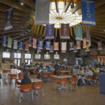 Students sit at tables eating lunch in a round room with wooden rafters and a round stained glass window in the center.
