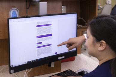 A woman looks at a computer monitor while a hand points at some text in a purple chat bubble.