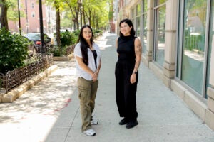 Two female students stand next to each other smiling.