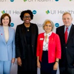 Three women and a man pose in front of a wall with the UI Health and UIC logos.