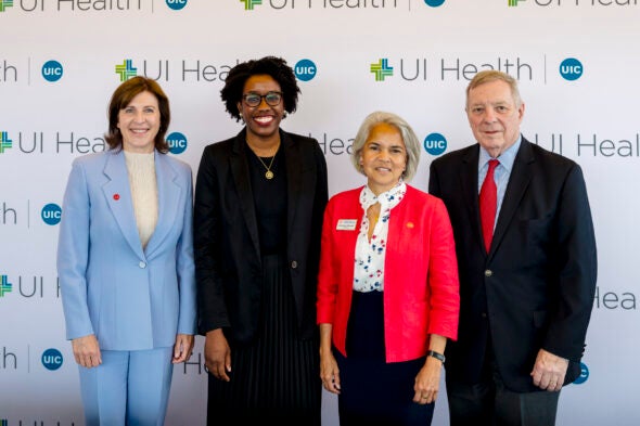 Three women and a man pose in front of a wall with the UI Health and UIC logos.