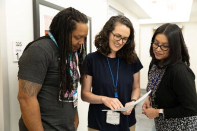 Three staff members look at papers together in the hallway of a doctor's office.