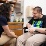 A doctor talks with a patient in a wheelchair.