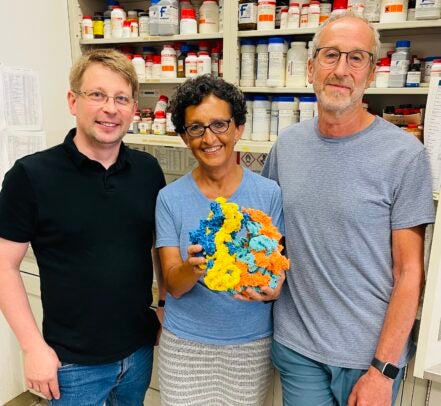 Two men and a woman stand in a laboratory. The woman is holding a 3D-printed ribosome in multiple colors.