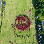 Aerial view of a large group of people in red shirts forming a circle mark with the letters "UIC" on a green field.