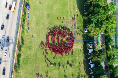 Aerial view of a large group of people in red shirts forming a circle mark with the letters "UIC" on a green field.