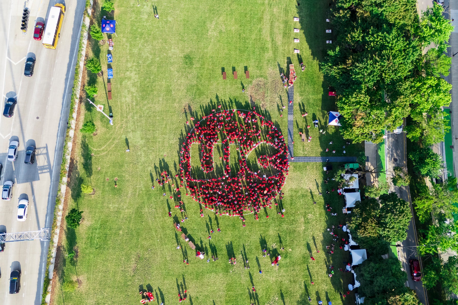 Aerial view of a large group of people in red shirts forming a circle mark with the letters "UIC" on a green field.