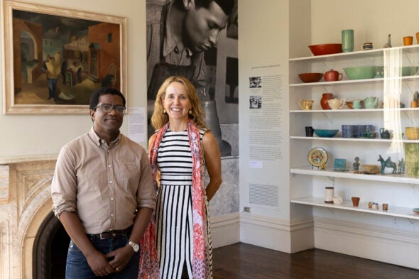 Two people stand in the Hull-House Museum in a room with photos on hte wall and old historic ceramics in bold colors.