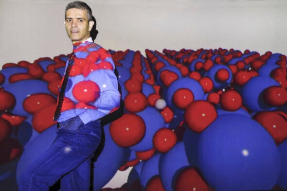 A man stands against a wall beneath a projection of red and blue balls.