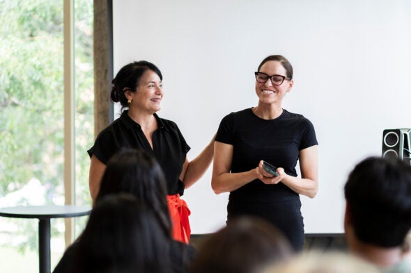 two women stand in front of an audience to accept an award.