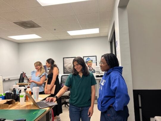 Two women look at a laptop in a classroom.