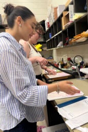 Two women fold zines and use a paper cutter.