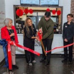 two people watch as two others cut a ribbon with giant scissors