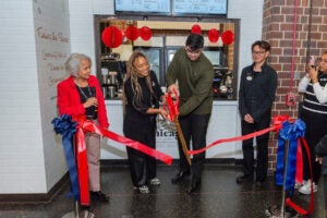 two people watch as two others cut a ribbon with giant scissors