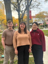 A man and two women pose outdoors on the UIC campus with trees in the background.