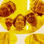 Five people in hair caps and gowns look down at the camera through a circular lens with a yellow tint.