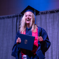 A graduate smiles on stage with her diploma.