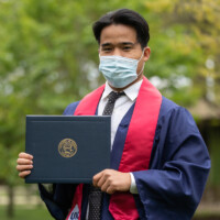 Graduate Bu Reh displays his diploma on campus .