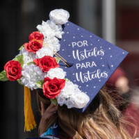 A graduation cap adorned with flowers and the phrase "Por ustedes para ustedes""