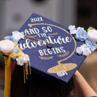 A graduation cap adorned with flowers and the phrase "And so the adventure begins"